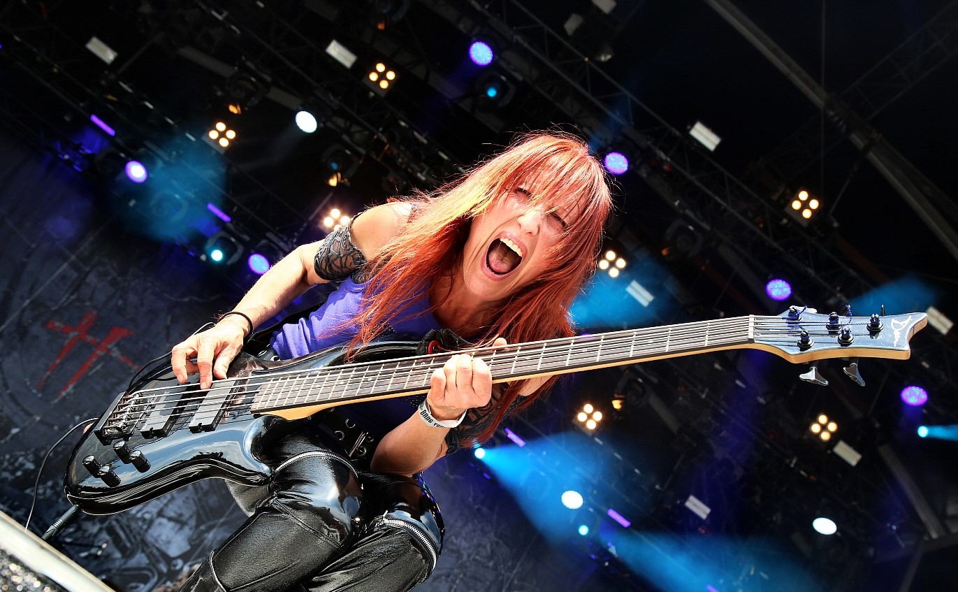 Enid Williams on stage playing guitar and shouting at camera